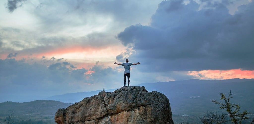 Photo of a man stood on a hilltop with his arms wide open