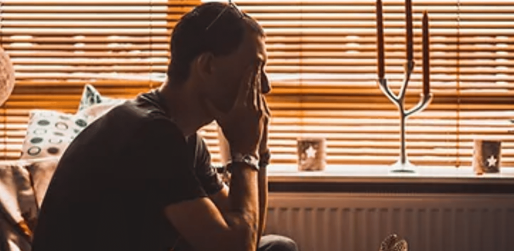 Photo of a man sat on a sofa with his hands holding his face