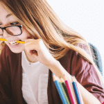 Image of lady sat at a desk with a pencil clenched between her teeth, looking at a laptop screen.